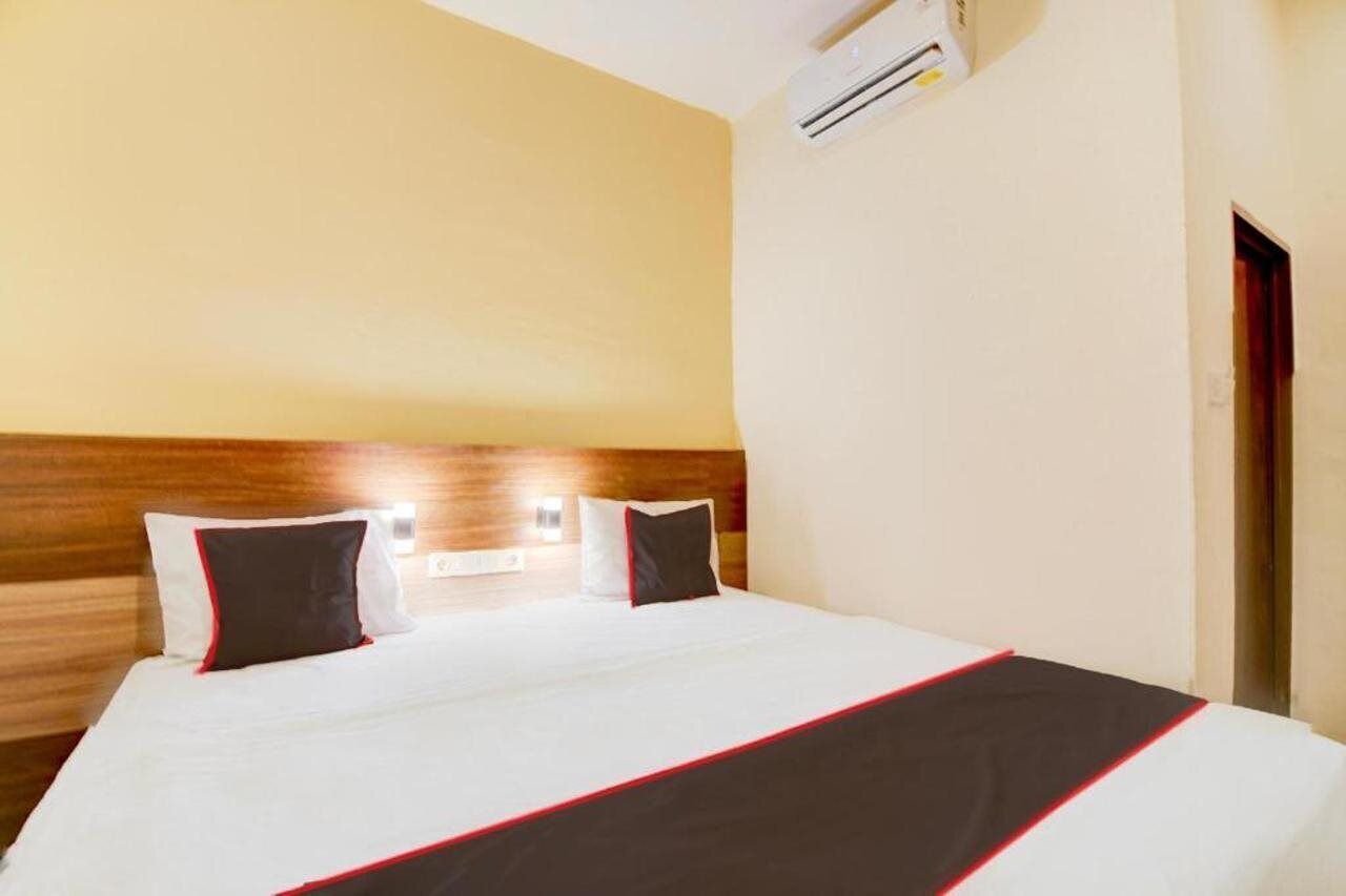 Una habitación de hotel con una cama, cabecera de madera, unidad de aire acondicionado y una puerta.