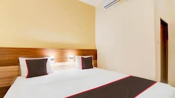 A hotel room with a bed, a wooden headboard, an air conditioning unit, and a door.