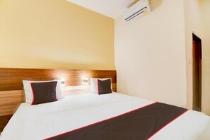 A hotel room with a bed, a wooden headboard, an air conditioning unit, and a door. - Capital O Pusat Kota Pekanbaru Near Mall Living World Formerly Radja Homestay (Tengkerang Barat)