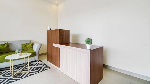 A modern reception area with a wooden desk, a white vase with a plant, and a green sofa with a patterned rug. - Capital O Pusat Kota Pekanbaru Near Mall Living World Formerly Radja Homestay (Tengkerang Barat)