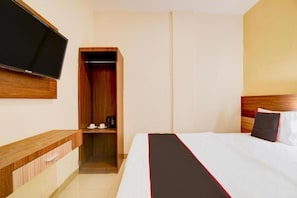 A hotel room with a bed, a TV mounted on the wall, a wooden wardrobe, and a bedside table. - Capital O Pusat Kota Pekanbaru Near Mall Living World Formerly Radja Homestay (Tengkerang Barat)