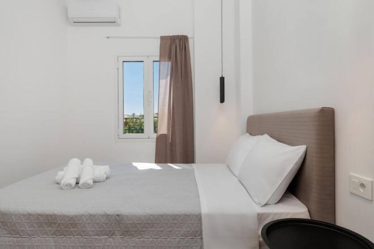 Ein Hotelzimmer mit Bett, einem Vorhangfenster, einer Wand-Klimaanlage und einem Nachttisch.