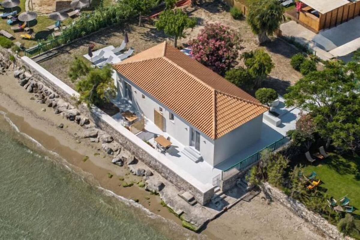A coastal building with a tiled roof, adjacent to a beach with lounge chairs and umbrellas.