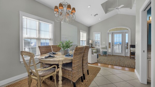 A spacious dining area with a round table, wicker chairs, and a chandelier.