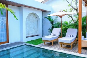 A poolside area with two lounge chairs, a stone wall, and a pergola with a table. - Villa Moon Orchid - 3 bedroom villa (Bali)