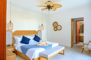 Un dormitorio con cama, mesitas de noche, ventilador de techo y una puerta que da a otra habitación.