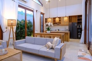 Una sala de estar moderna con sofá, comedor y cocina con alacenas de madera y un refrigerador.
