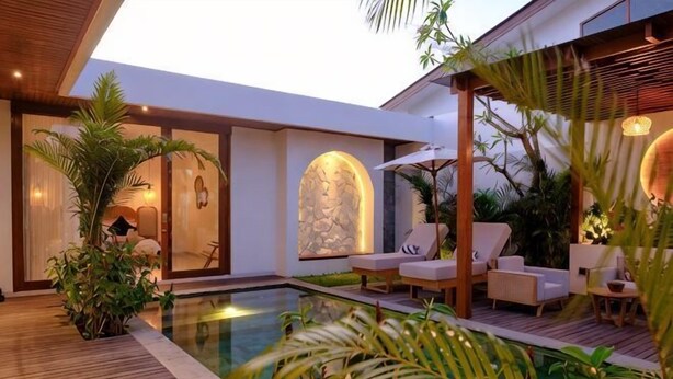 A modern outdoor pool area with lounge chairs, a wooden deck, and tropical plants.