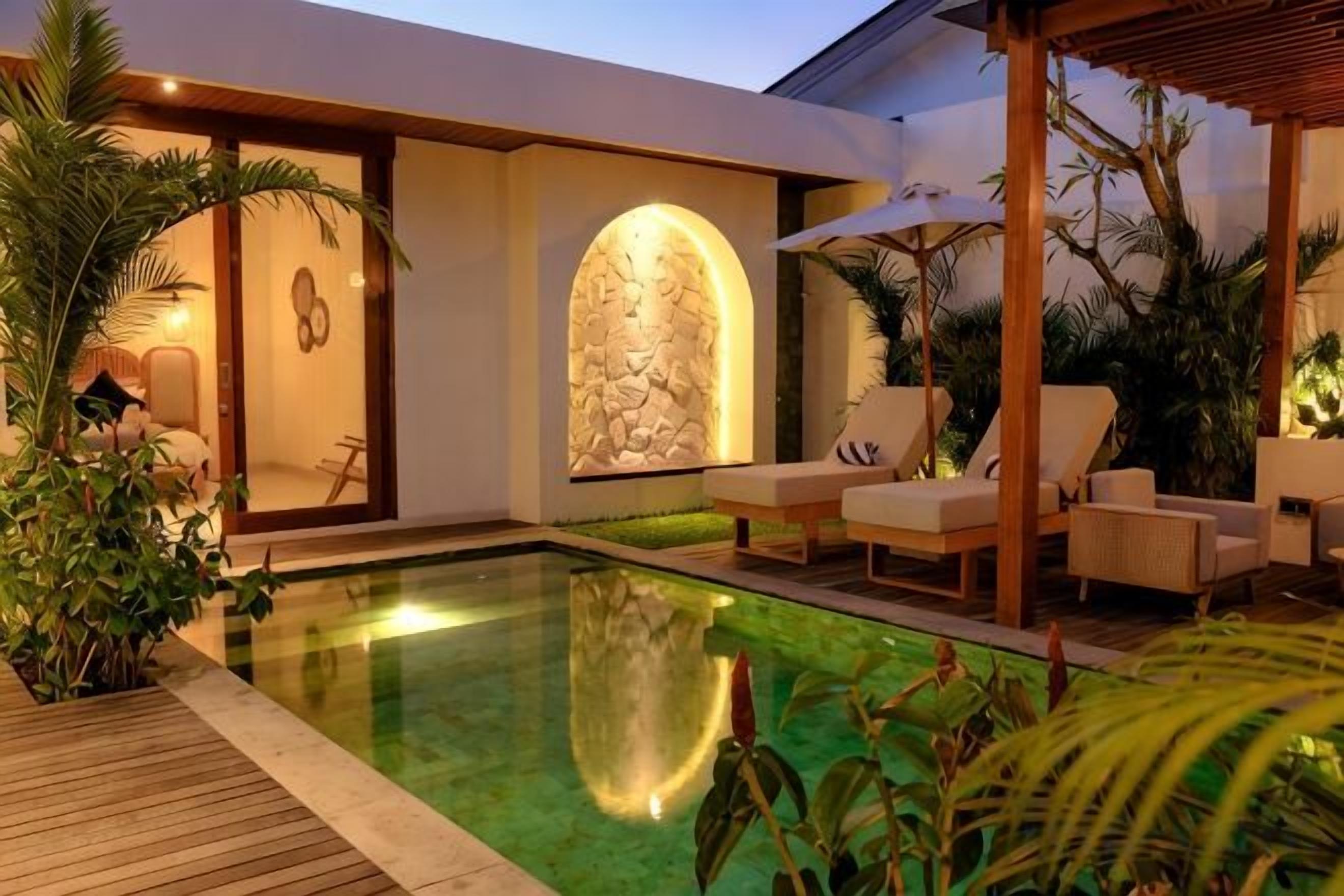 Un espace piscine extérieur moderne, doté de chaises longues, d’un mur en pierre et de plantes tropicales.