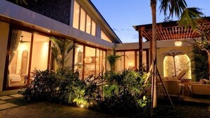 A modern building with large windows, a covered outdoor seating area, and lush greenery.