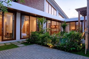 Een modern gebouw met grote glasramen, een betegeld terras en weelderige begroeiing.
