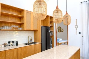 A modern kitchen with wooden cabinetry, a black refrigerator, and wicker pendant lights. - Villa Moon Orchid - 3 bedroom villa (Bali)