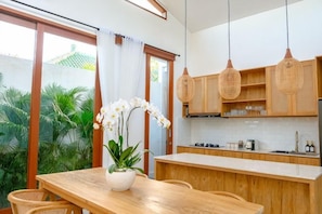 Una cocina moderna con armarios de madera, una mesa de comedor con sillas y una orquídea en maceta.