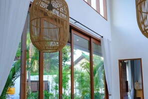 Una habitación con ventanas amplias, una lámpara de techo tejida y vistas al verde exterior.
