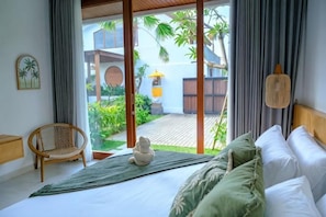 Un dormitorio con cama, una silla, una mesita y vistas al exterior.