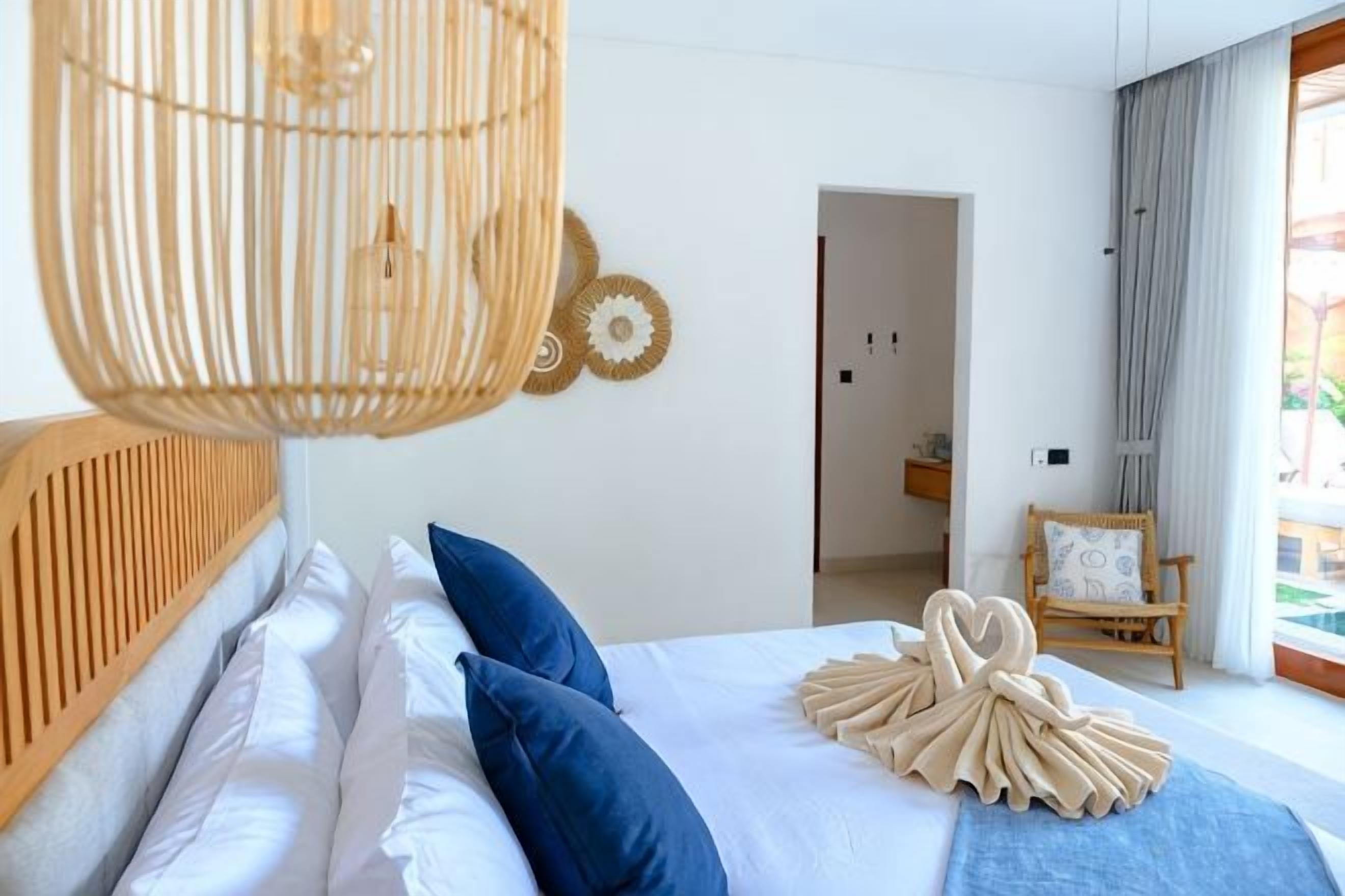 Une chambre à coucher avec un lit, un luminaire suspendu, une tête de lit en bois et une vue sur l’extérieur.