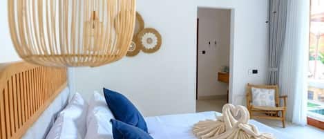 Ein Schlafzimmer mit Bett, einer Pendelleuchte, einem hölzernen Kopfteil und Blick ins Freie.