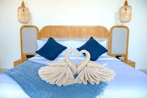 Een bed met een houten hoofdbord, twee blauwe kussens, een blauwe deken en twee handdoeken in de vorm van zwanen.