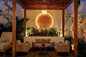 A covered outdoor seating area with a round light fixture, wicker furniture, and lush plants. - Villa Moon Orchid - 3 bedroom villa (Bali)