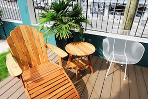 Une terrasse en bois avec une chaise en bois, une petite table ronde et une chaise en métal blanche.