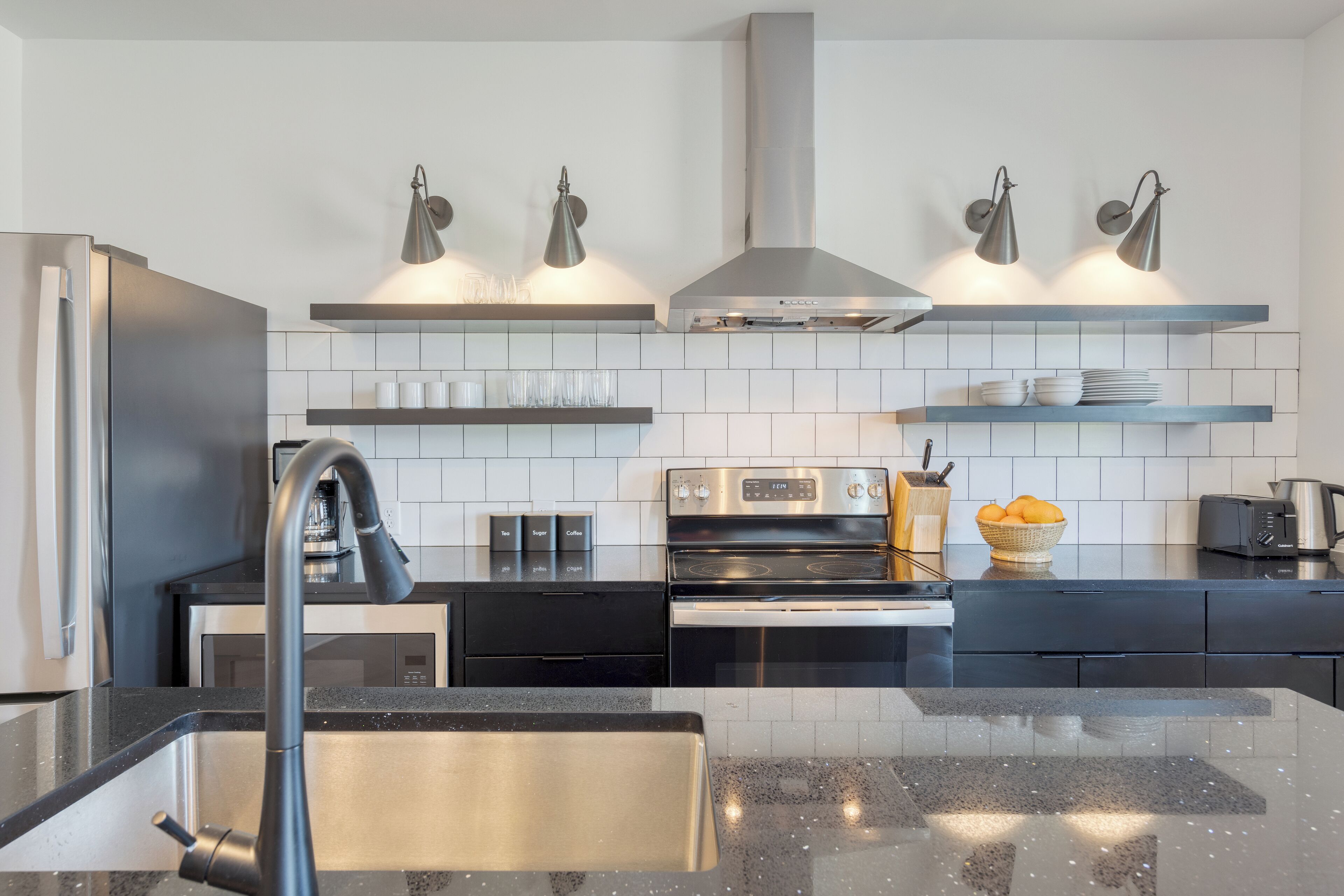 A modern kitchen with a stainless steel refrigerator, black countertops, a built-in oven, and a gas range.