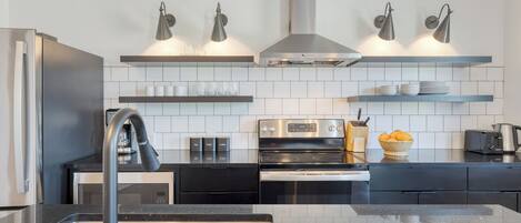 A modern kitchen with a stainless steel refrigerator, black countertops, a built-in oven, and a gas range.