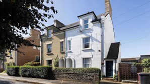 A two-story residential building with a white facade, a small front garden, and a visible garage door. - Characterful City Maisonette for 4 (Chichester)