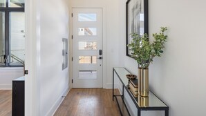Un pasillo con una puerta blanca, un cuadro en la pared y una consola con una planta.