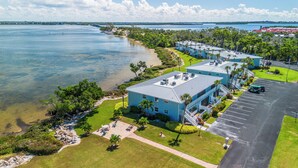 A coastal hotel with multiple blue buildings, a parking lot, and a view of the sea. - West Bay Cove 242 · Murphy Bed Office · Pool (Holmes Beach)
