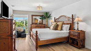 A bedroom with a large bed, wooden furniture, a television, and a view of greenery outside. - West Bay Cove 242 · Murphy Bed Office · Pool (Holmes Beach)