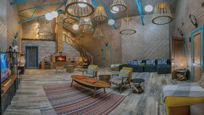 Un vaste espace de vie doté d’une cheminée, de sièges confortables et de plusieurs luminaires suspendus.