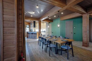 A dining area with a long table, chairs, and a kitchen in the background.