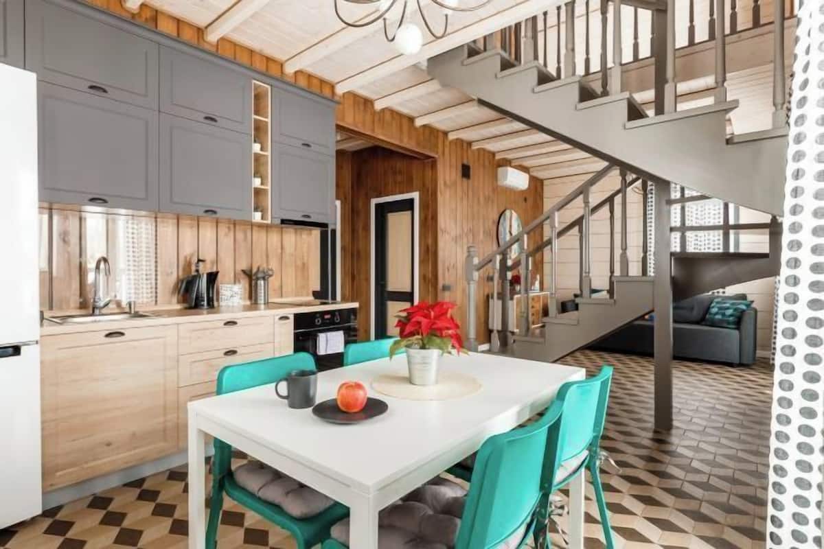 Een moderne keuken met grijze kastjes, een witte eettafel en blauwgroene stoelen.