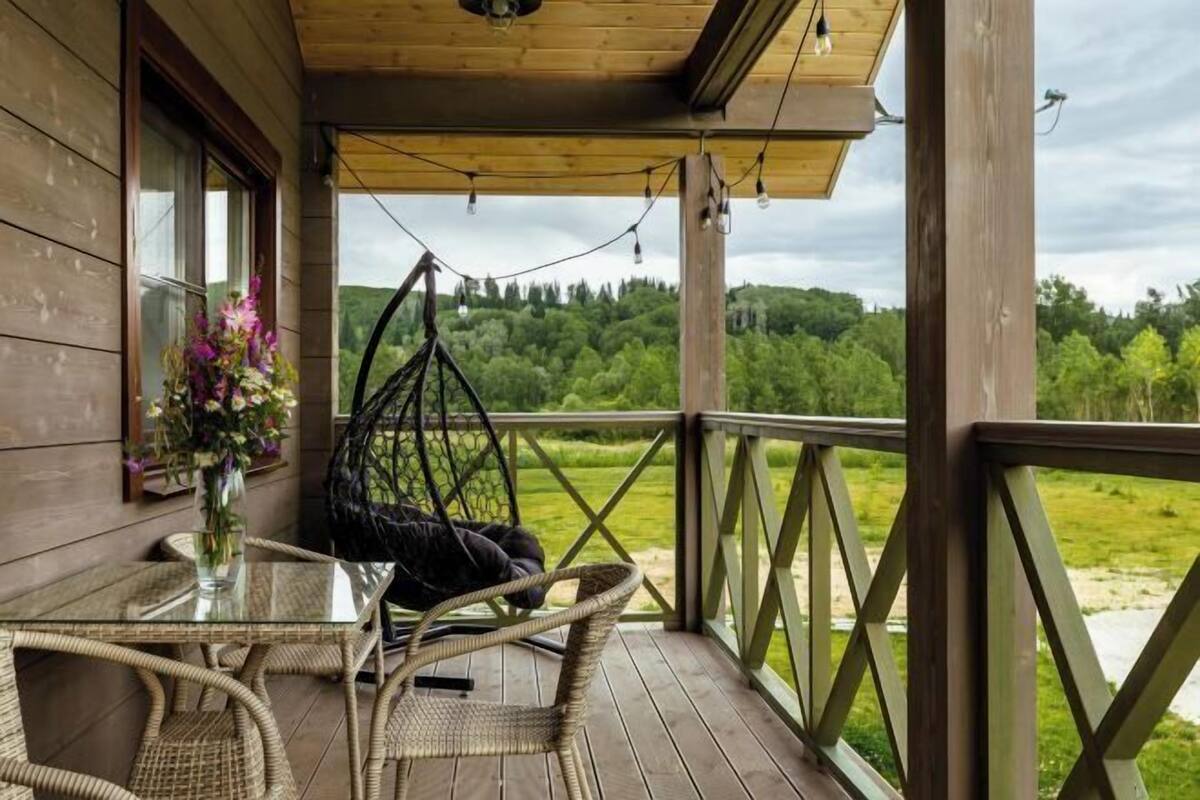 Een houten terras met rieten meubels, een hangstoel en een glazen tafel.