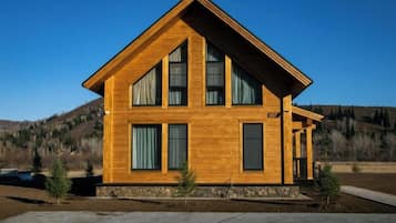 Une maison en bois à deux étages, dotée d’un toit à pignon, de grandes fenêtres et de fondations en pierre.