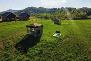 Una propiedad rural con varias construcciones, incluyendo una casa grande y estructuras más pequeñas, ubicada en un campo cubierto de hierba con colinas al fondo.