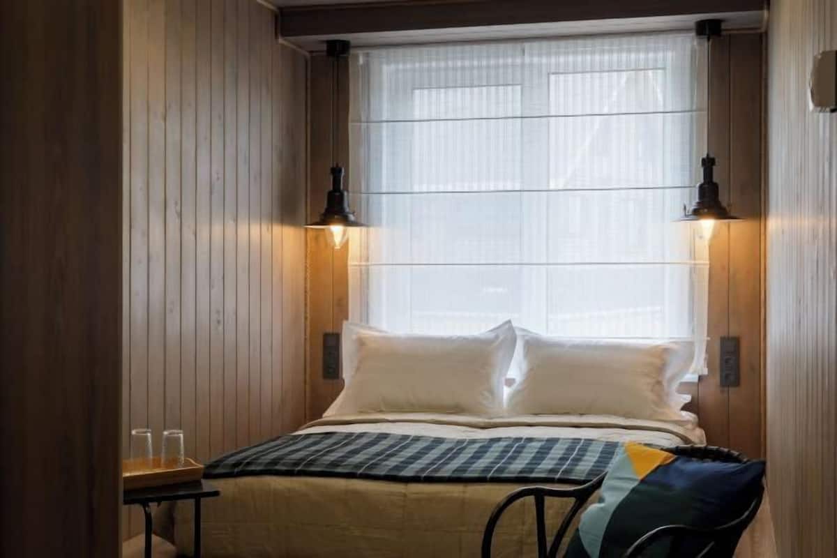 Een gezellige kamer met een bed, twee wandlampen en een raam met jaloezieën.