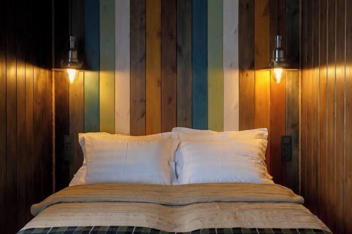 Een bed met witte lakens, een houten hoofdbord en twee wandlampen.