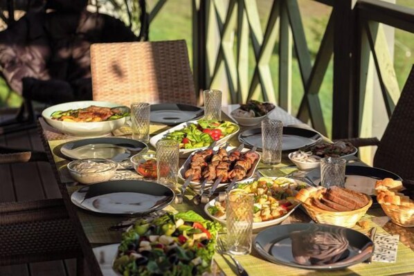 Una mesa de comedor al aire libre con diversos platos y bebidas, rodeada de sillas de mimbre.