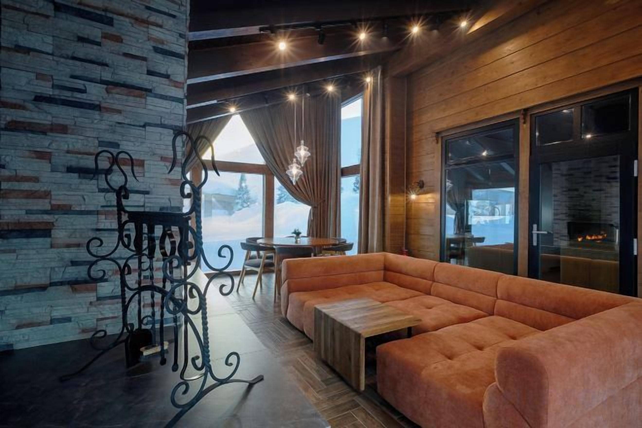 A cozy room with a brick wall, a cushioned seating area, a wooden table, and a large window with curtains.