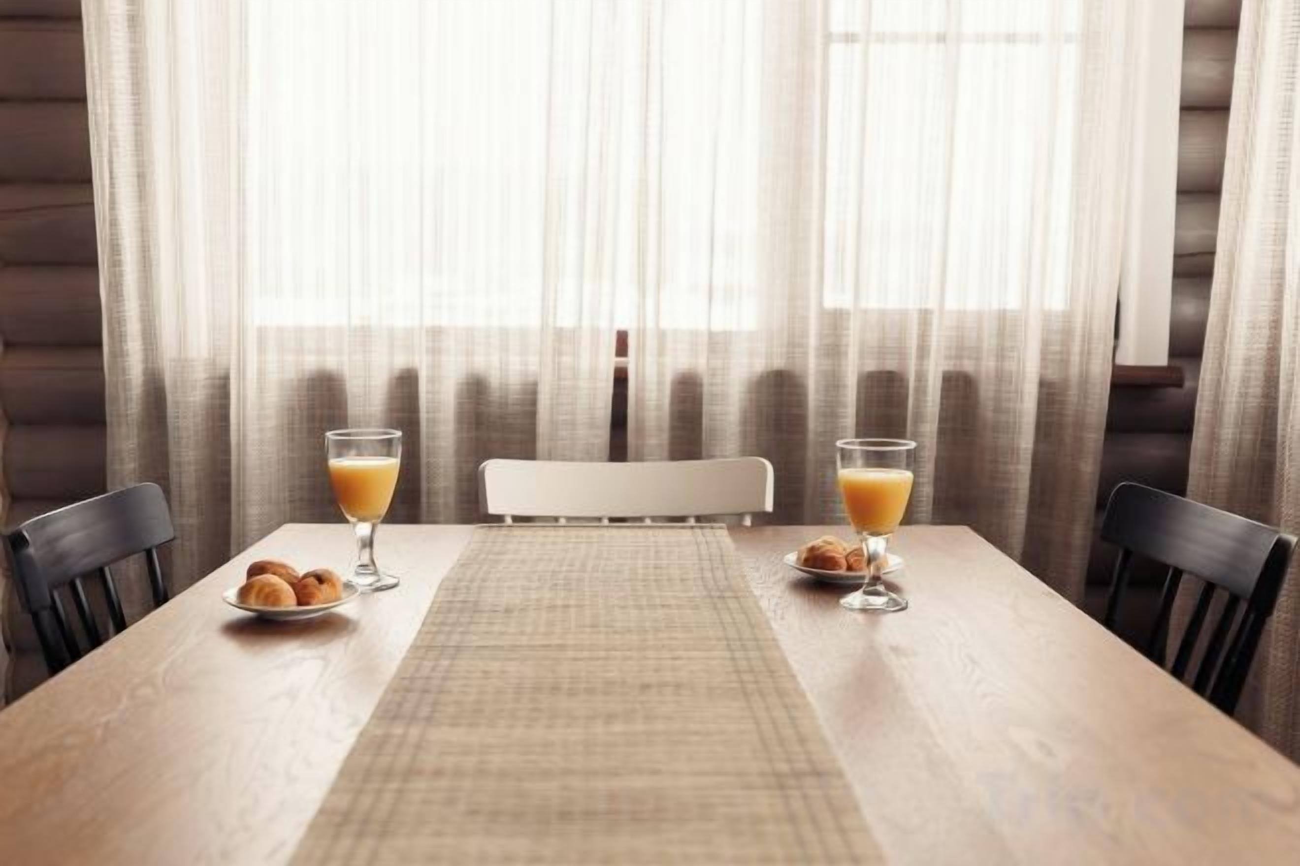 Een houten eettafel met twee stoelen, een placemat en twee glazen sinaasappelsap.