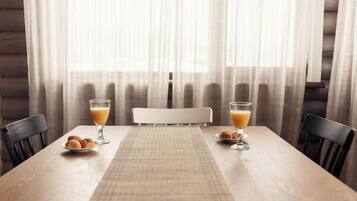 Een houten eettafel met twee stoelen, een placemat en twee glazen sinaasappelsap.