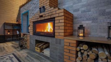 A fireplace with a visible fire, a stack of firewood, and a blue door.
