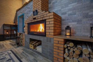 Una chimenea con fuego encendido, un montón de leña y una puerta azul.