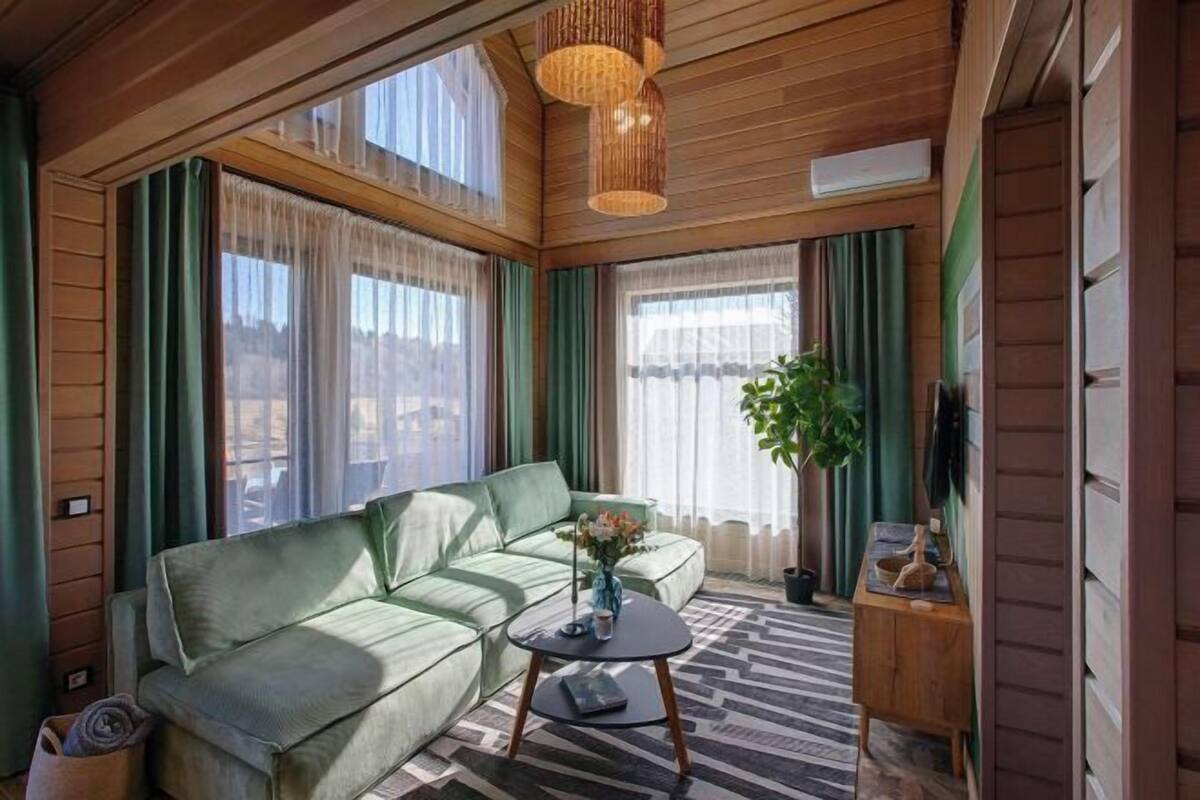 Een gezellige kamer met een groene bank, een klein tafeltje met een vaas en een hanglamp.