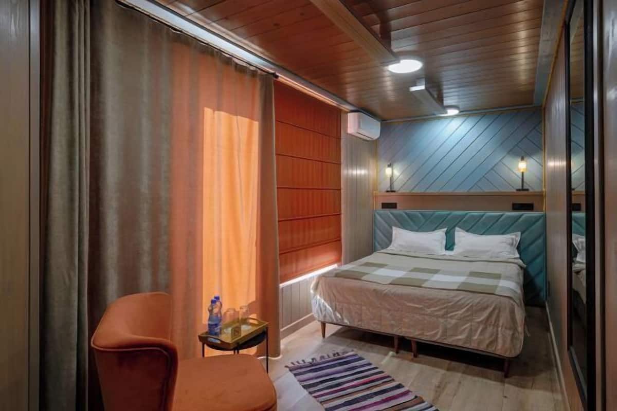 Een hotelkamer met een bed, een stoel, een klein tafeltje met een fles en een gestreept vloerkleed.