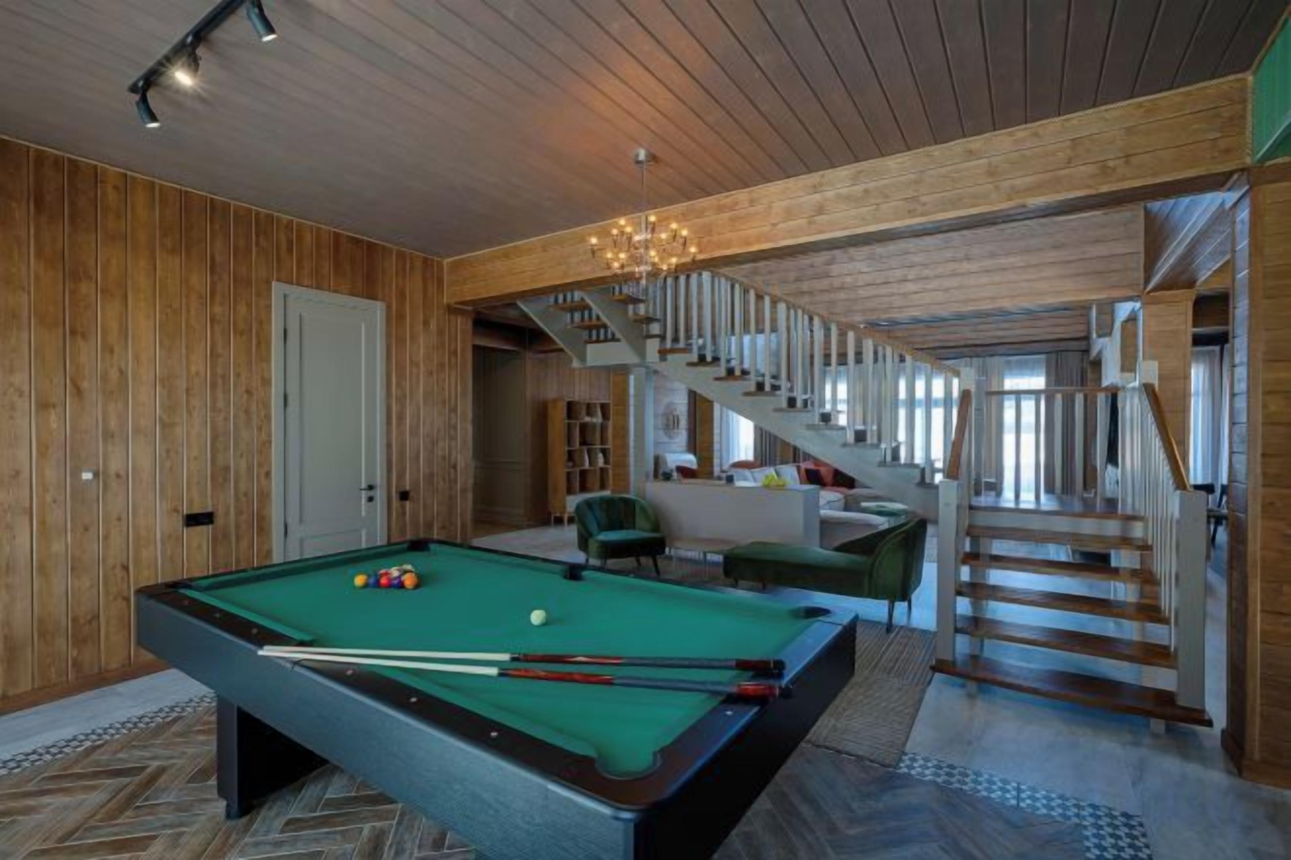 A pool table in a room with wooden walls and a staircase leading to another level.