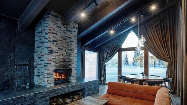 Un salon moderne avec une cheminée en pierre, un canapé en cuir et une vue sur un paysage enneigé.
