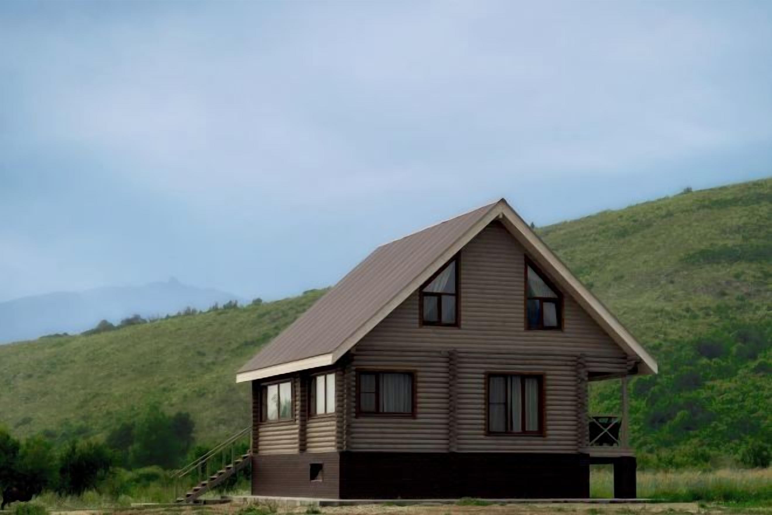 Een gelijkvloers houten huis met een puntig dak, een veranda en een trap naar de ingang.