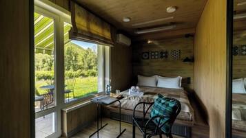 Een kamer met een bed, een tafel en een stoel. Er is een raam met uitzicht op groen.